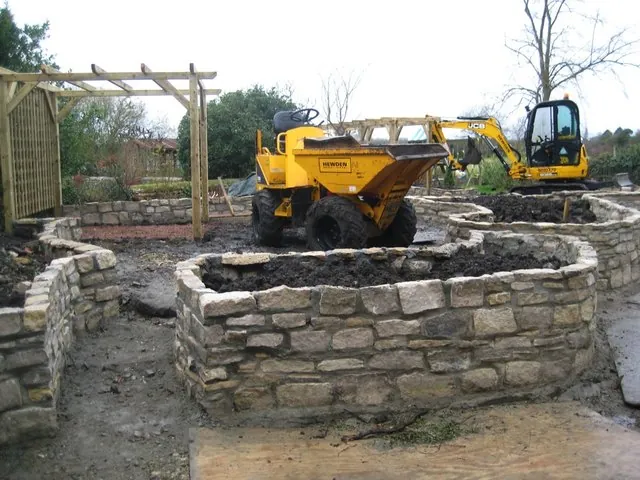 Stone walls being built, with a dumper and digger on site
